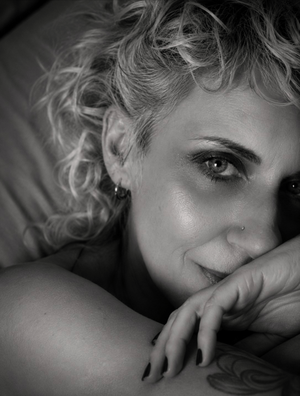 Primer plano en blanco y negro de una mujer recostada, con una mirada sugerente y sensual.